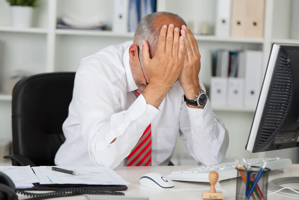 A man with hands over his head, stressing with hearing loss in the workplace.