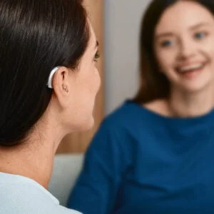 Young woman with hearing loss, wearing hearing aid having conversation with friend