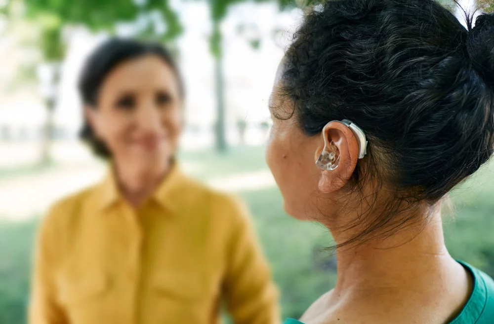 Adult woman with hearing loss uses a hearing aid to communicate with her female friend.