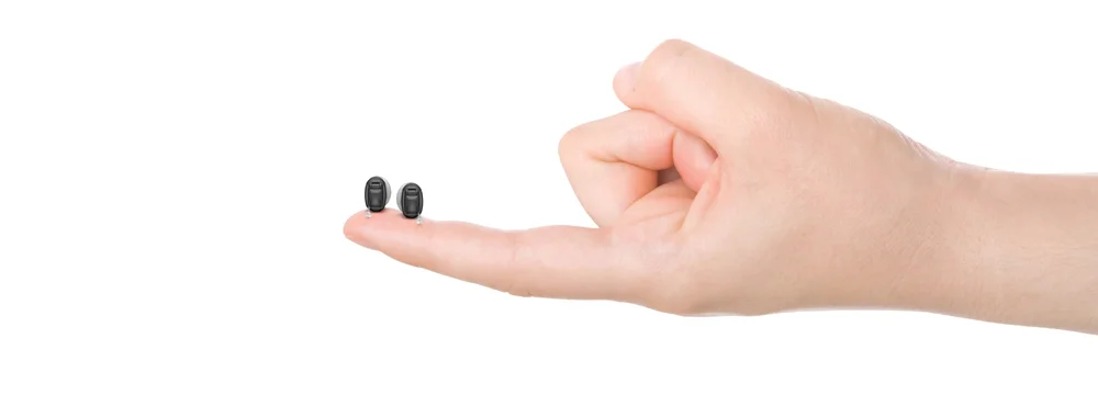 Two tiny hearing aids being held on one single finger