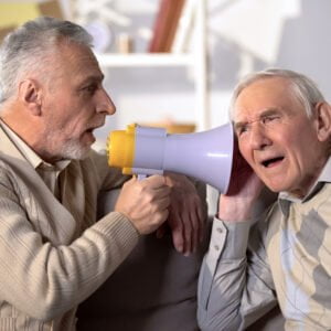 Middle-aged man using a megaphone to shout into the ear of hard of hearing conversation partner