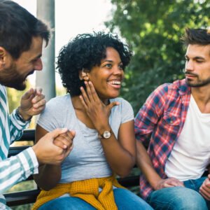 Young woman wearing a hearing loss with a hearing aid socialising with friends outdoors.