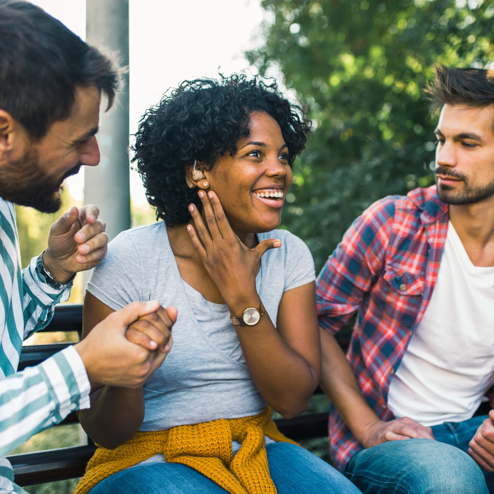 Young woman wearing a hearing loss with a hearing aid socialising with friends outdoors.
